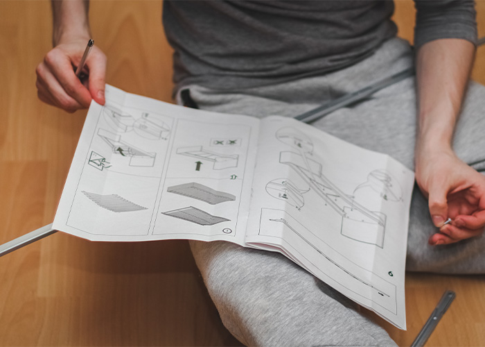 anleitung-pdf Person hält und betrachtet eine ausgedruckte Anleitung mit Illustrationen und Text.