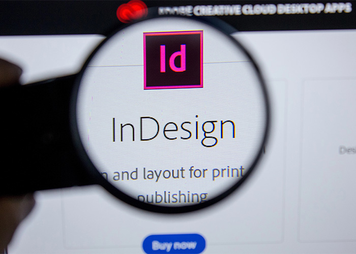 indesign-pdf Vergrößerte Ansicht des Adobe InDesign-Logos auf einem Bildschirm, dargestellt mit einer Lupe.