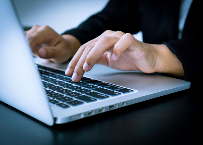 programme-pdf Hände tippen auf der Tastatur eines Laptops.